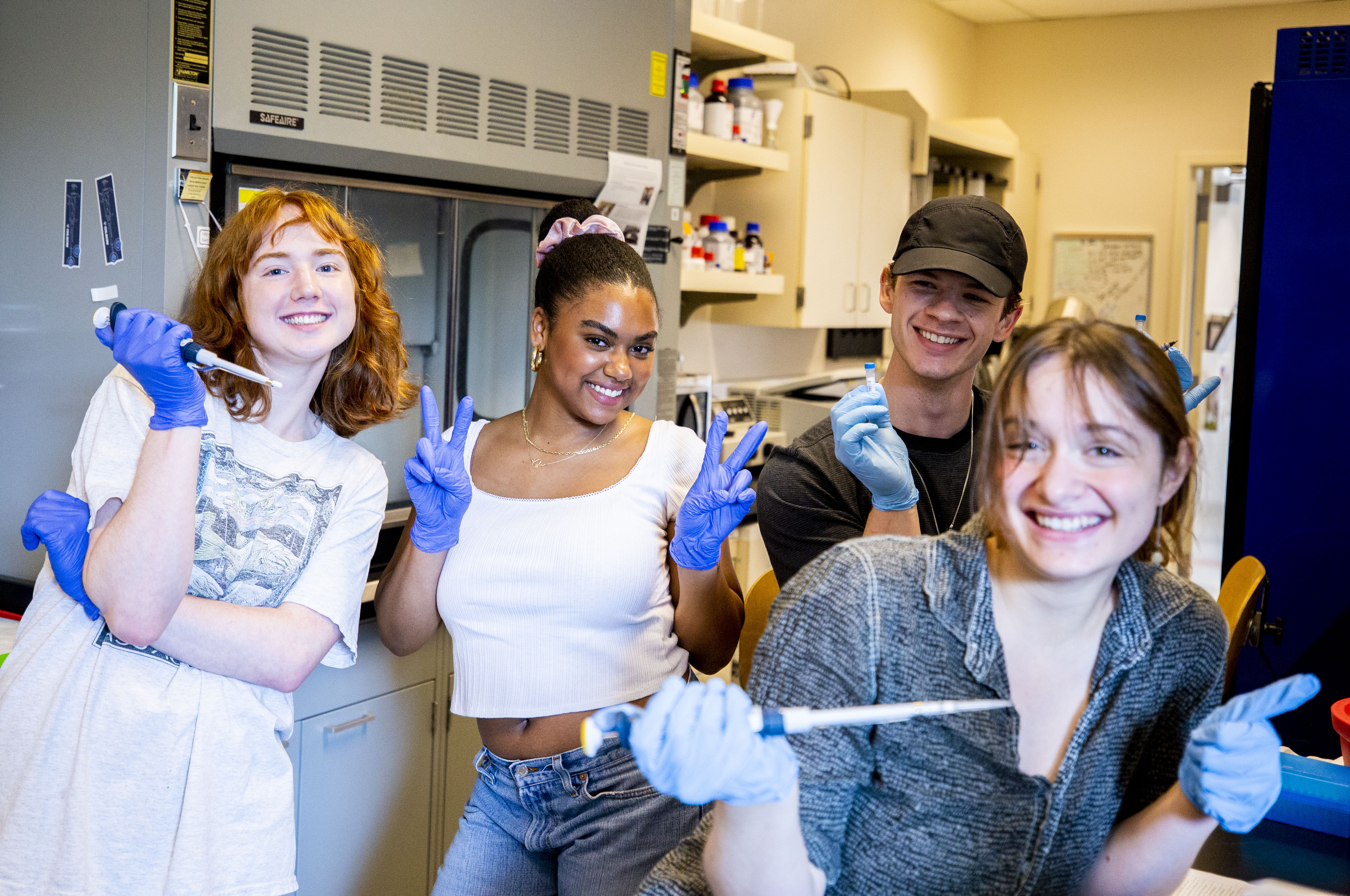 Four students pose for a photo with pipettes in a lab.