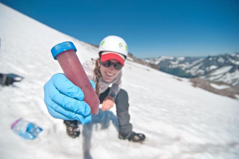 student holding tube of watermelon snow while crouching on a snowy mountain