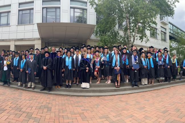 Graduates and faculty in commencement regalia stand on the front steps of the Biology building